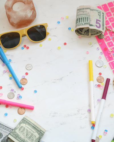 Markers, coins, sunglasses, and dollar bills on marble countertop
